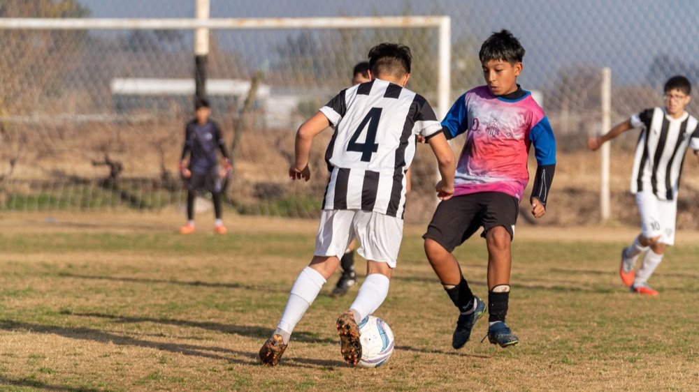 Crianças jogando futebol num campo de terra e grama